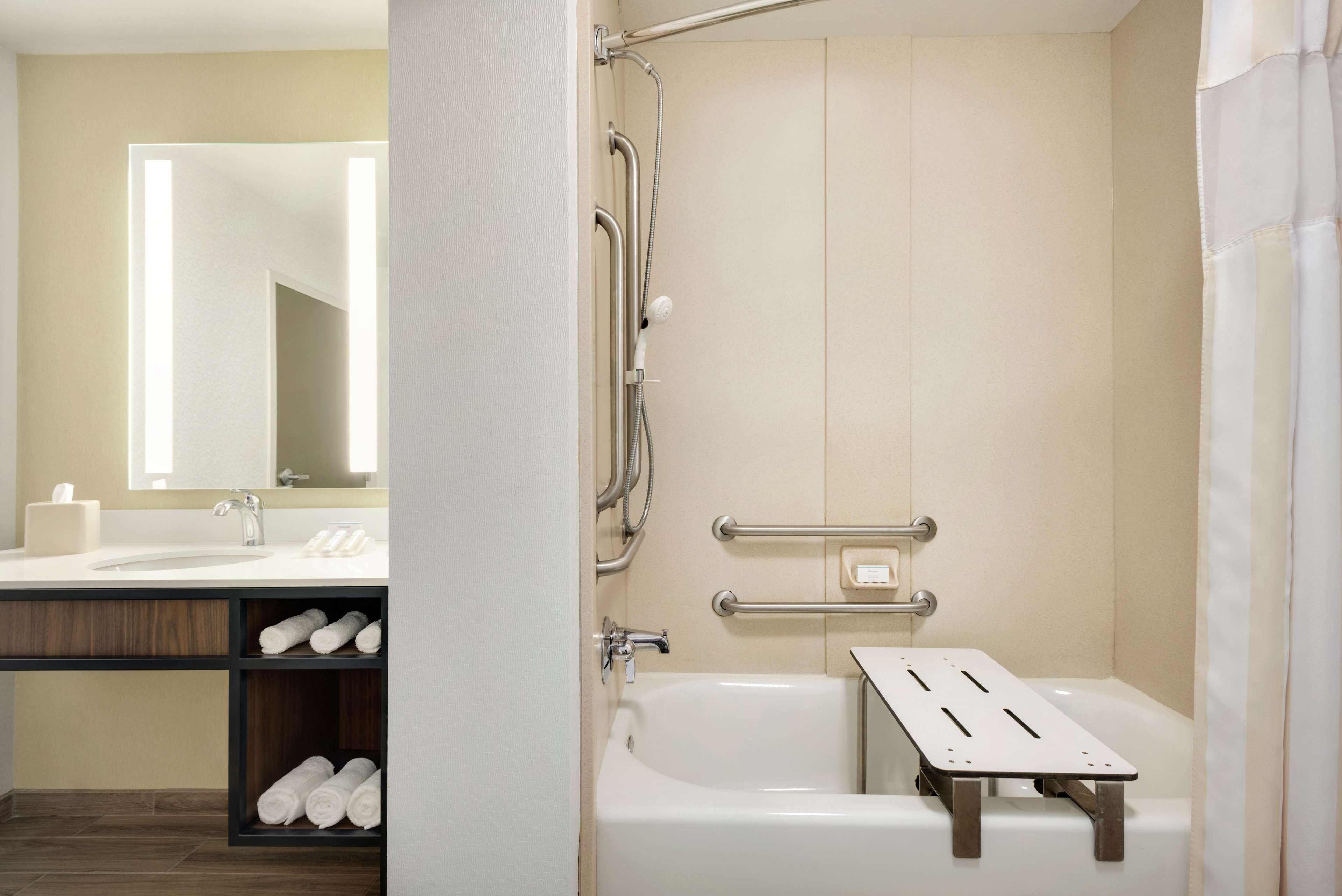 Een moderne badkamer met een badkuip, een douche met handgrepen, een wastafel met spiegel en een plank met handdoeken.