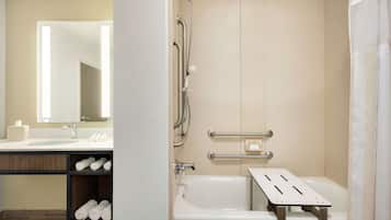 Een moderne badkamer met een badkuip, een douche met handgrepen, een wastafel met spiegel en een plank met handdoeken.