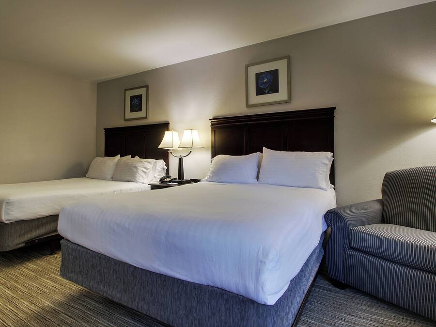 A hotel room with two single beds, a double bed, a chair, and a nightstand with a lamp.