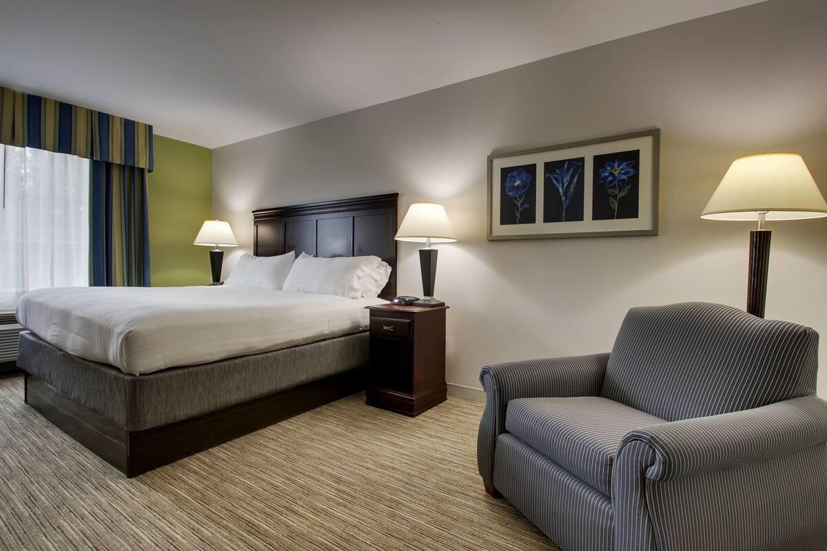 A hotel room with a bed, two bedside tables with lamps, a chair, and a wall with framed artwork.