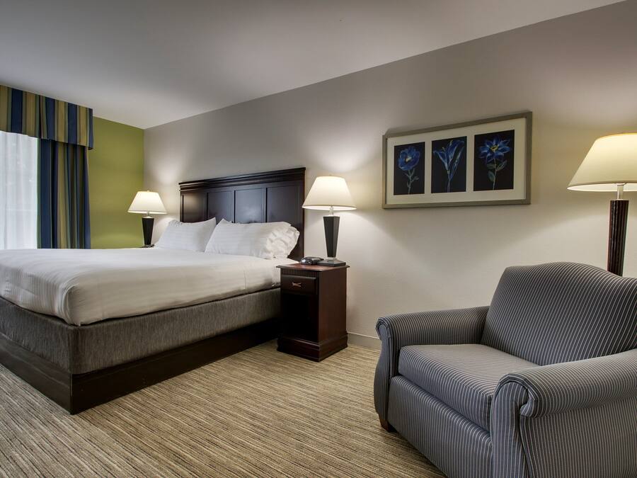 Una habitación de hotel con una cama, dos mesitas de noche con lámparas, una silla y una pared decorada con cuadros.