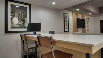 A modern kitchen with a white countertop, two bar stools, a computer, and a flat-screen TV mounted on the wall.