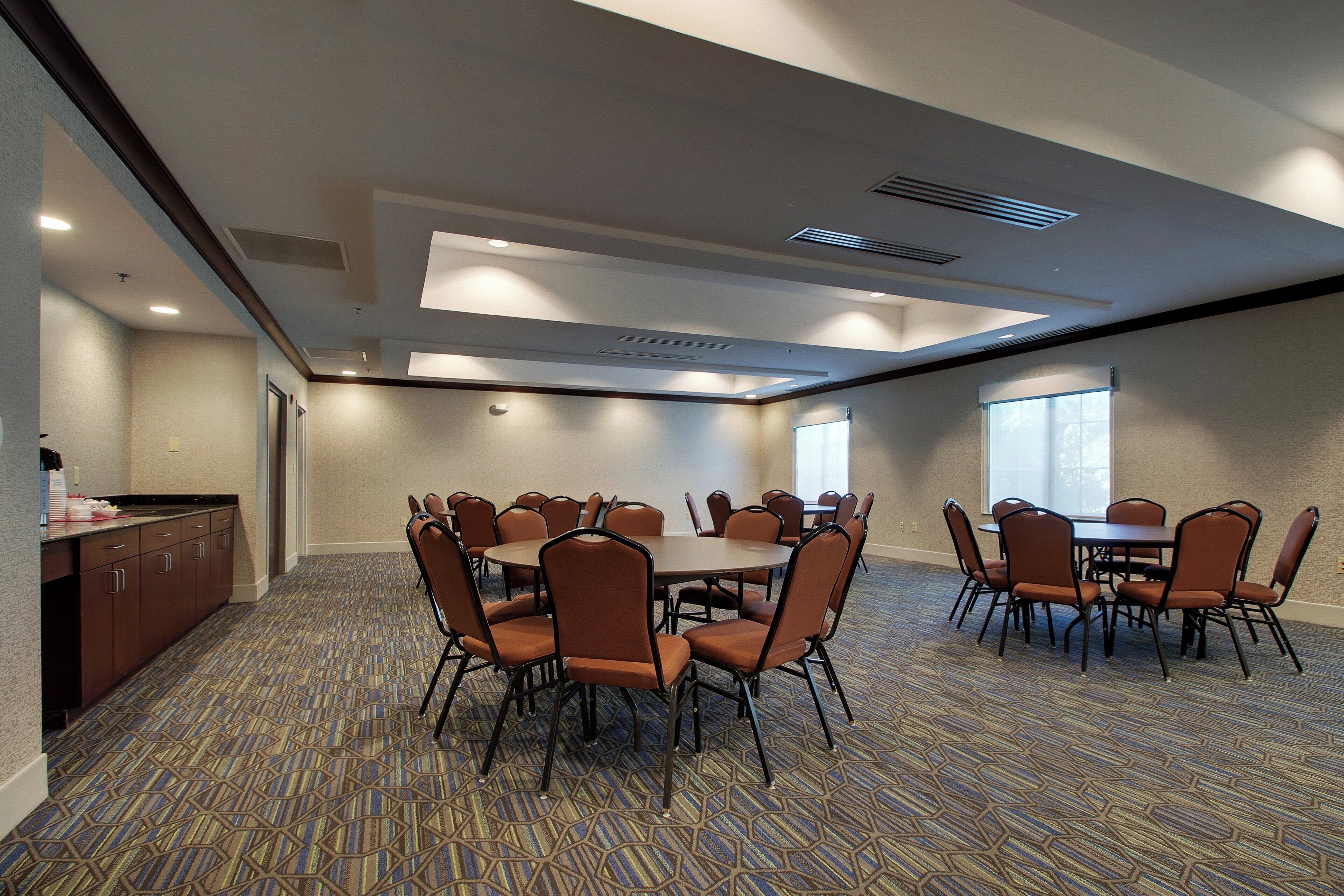 A conference room with a large table surrounded by chairs, a kitchenette, and a patterned carpet.