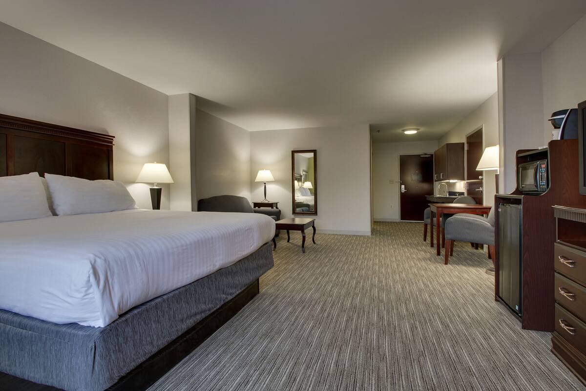A hotel room with a large bed, a desk with a chair, a microwave, and a refrigerator.