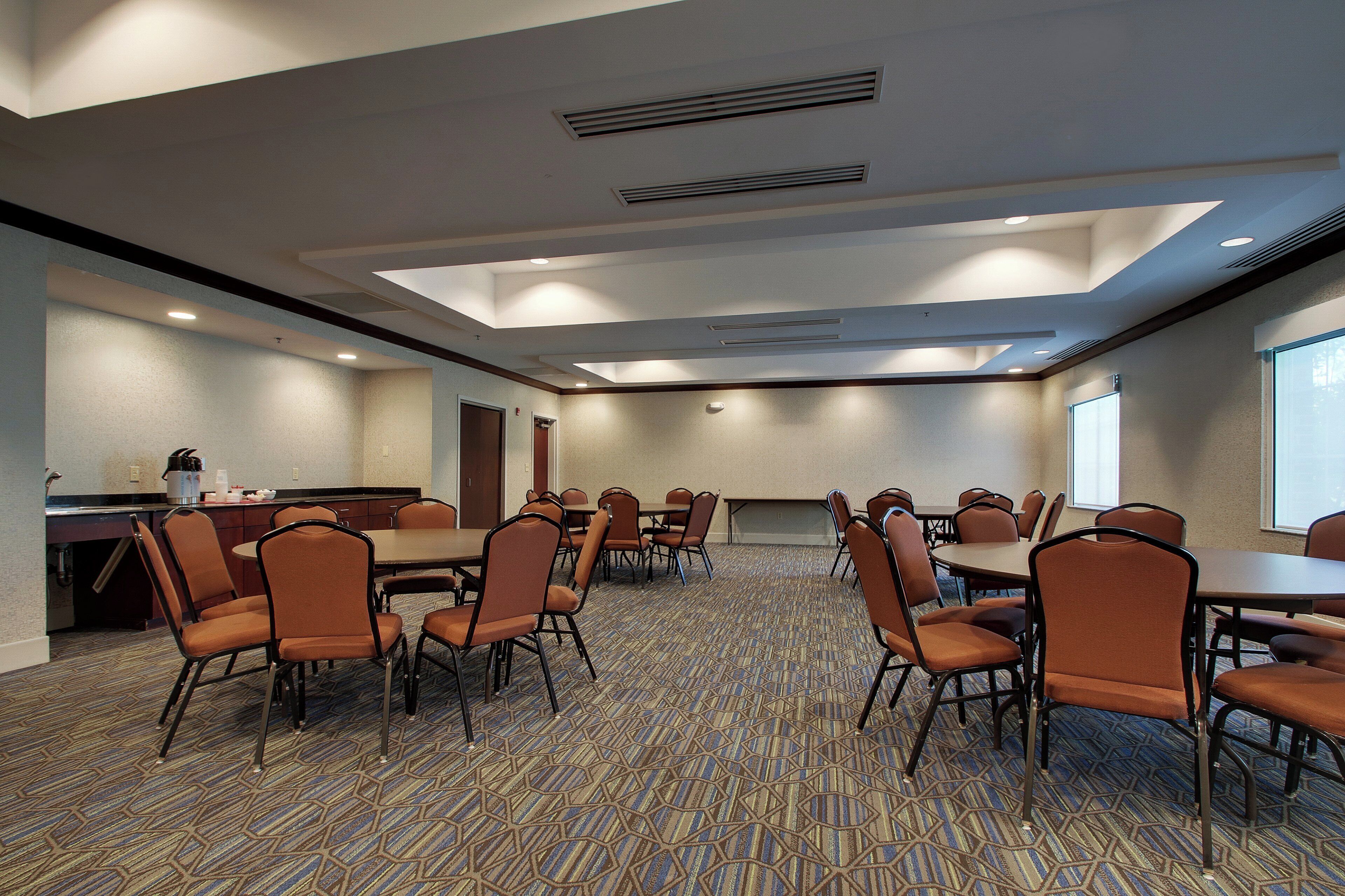 A conference room with multiple tables and chairs, a kitchenette, and a patterned carpet.