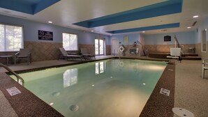 Une piscine intérieure équipée de chaises longues, d’un poste de surveillance pour le sauveteur et d’un panneau indiquant qu’il est interdit de plonger.