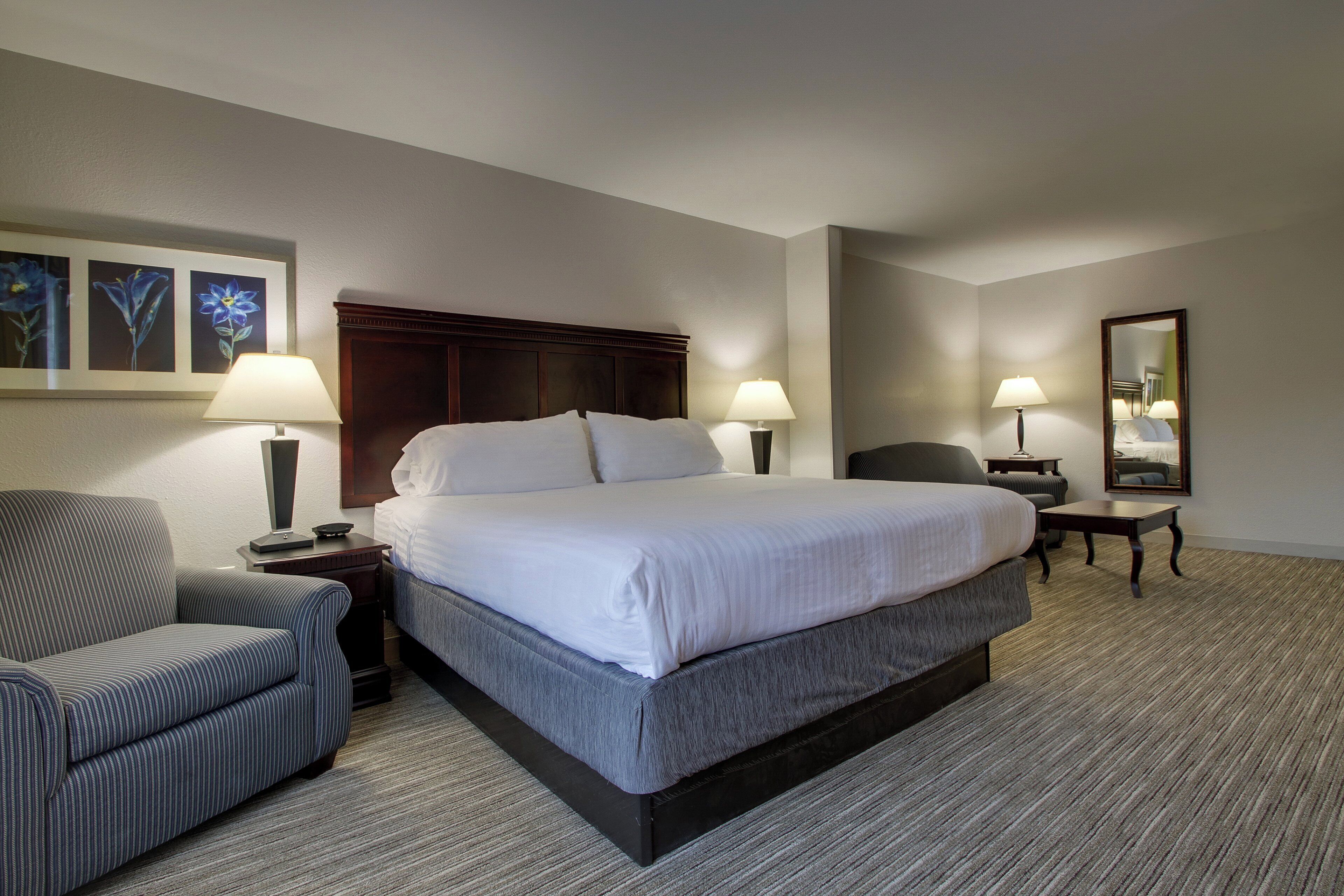 A hotel room with a large bed, two bedside tables with lamps, a chair, a desk, and a mirror.