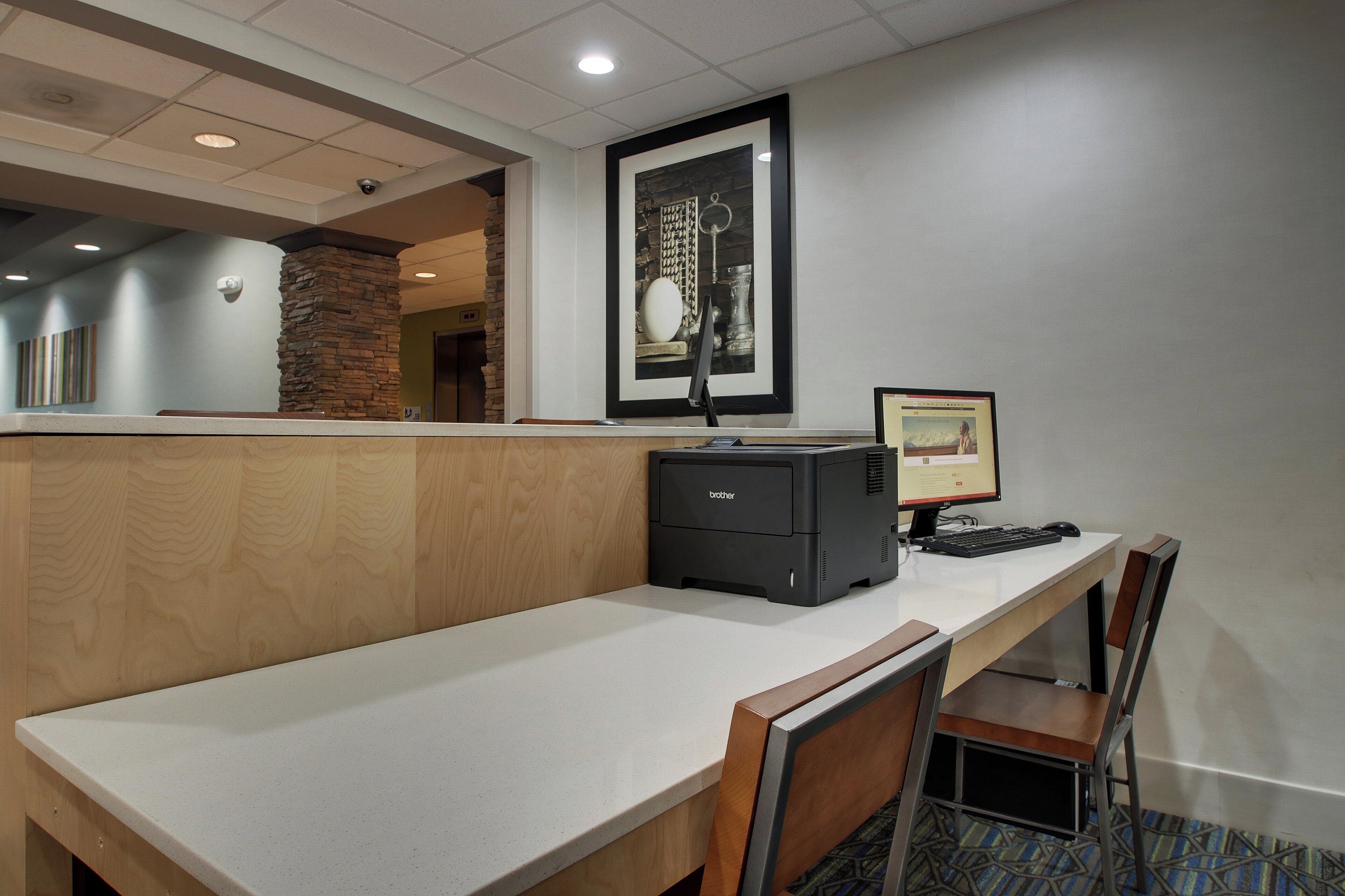 A hotel reception desk with a computer, a printer, and a framed picture on the wall.