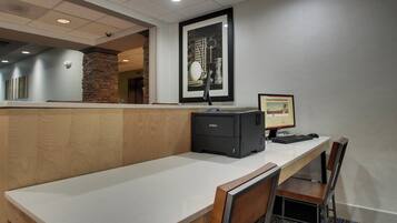 A hotel reception desk with a computer, a printer, and a framed picture on the wall.