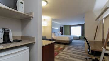 A hotel room with a bed, a desk with a coffee maker, a chair, and a lamp.