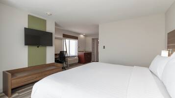 A hotel room with a large bed, a desk with a chair, a flat-screen TV mounted on the wall, and a window with curtains.