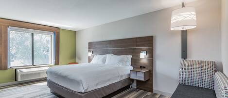 Une chambre d’hôtel moderne avec un grand lit, des tables de chevet, un banc et une fenêtre donnant sur un beau paysage.