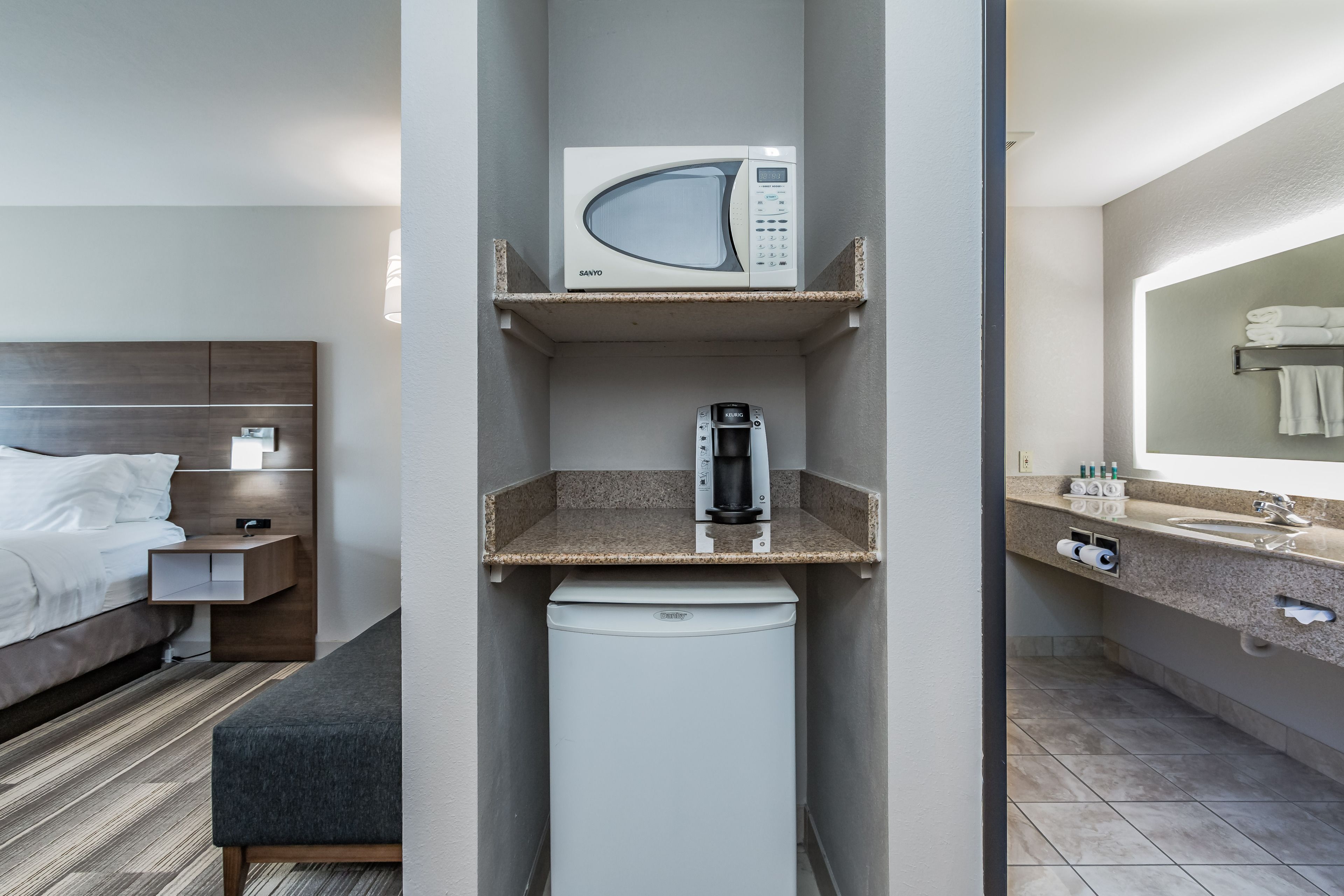 Une chambre d’hôtel compacte comprenant un lit, une petite kitchenette équipée d’un four à micro-ondes, d’une machine à café et d’un mini-réfrigérateur.
