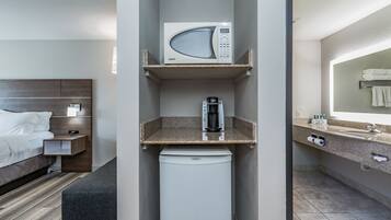 A compact hotel room with a bed, a small kitchenette with a microwave, a coffee maker, and a mini-fridge.
