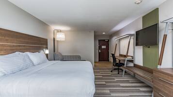 A hotel room with a large bed, a desk with a chair, a flat-screen TV, and a wooden dresser.