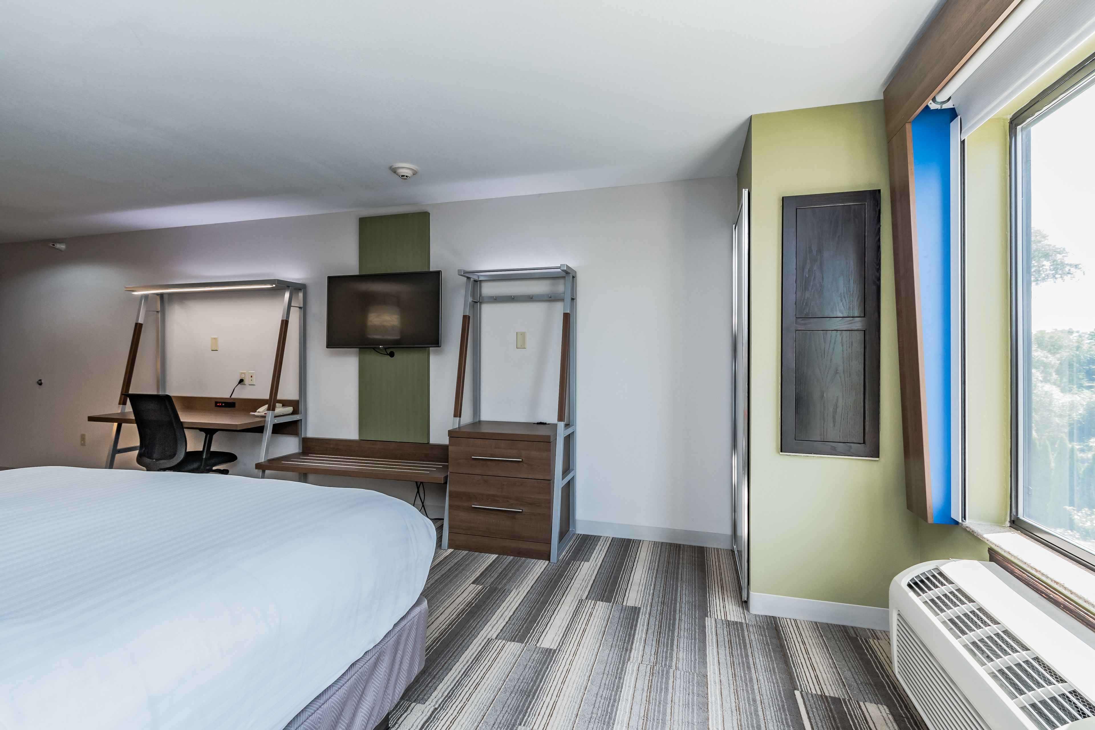 A hotel room with a bed, desk, chair, TV, and a window with a view.