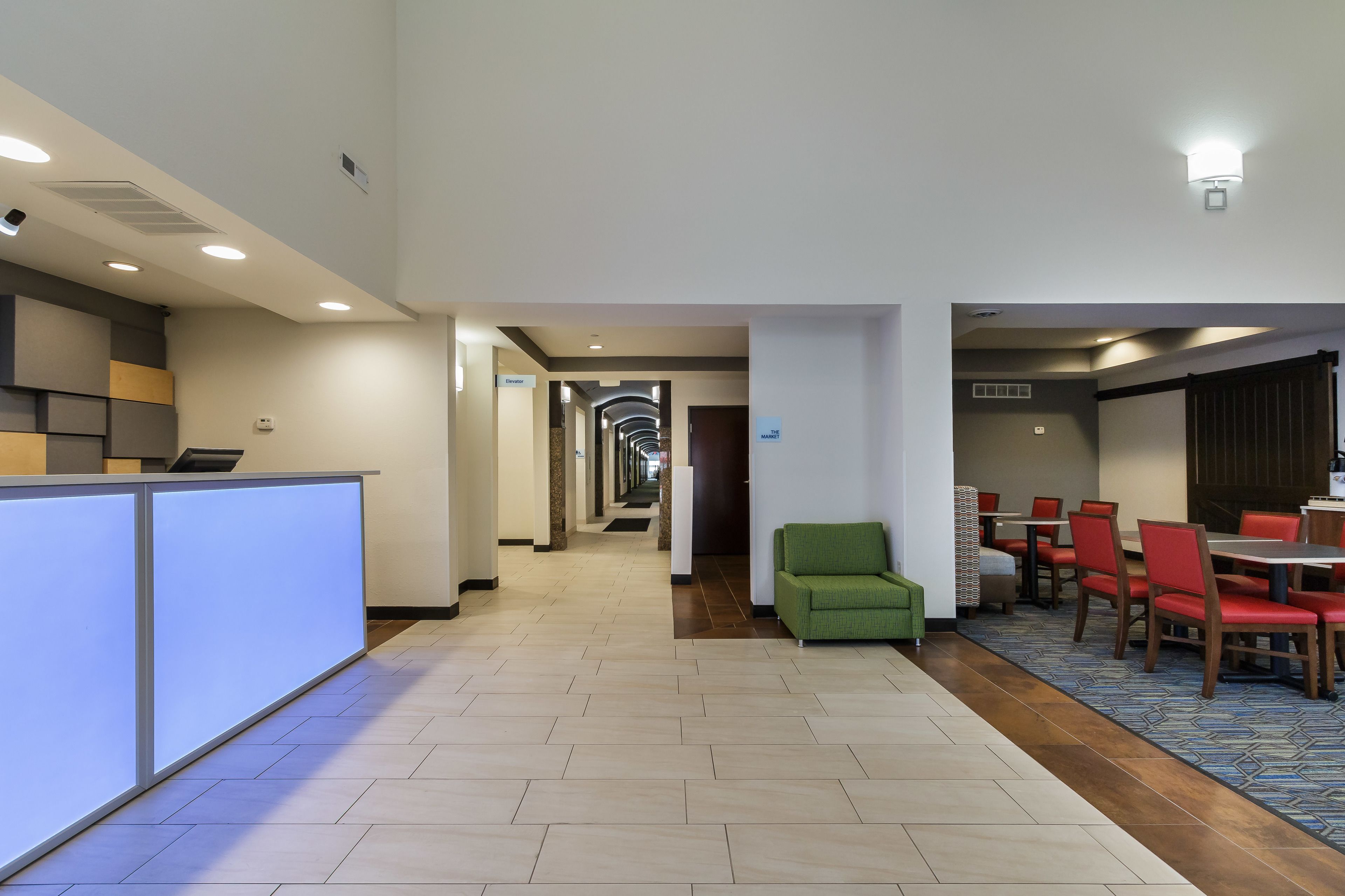 A hotel lobby with a reception desk, a green armchair, and a dining area with red chairs.