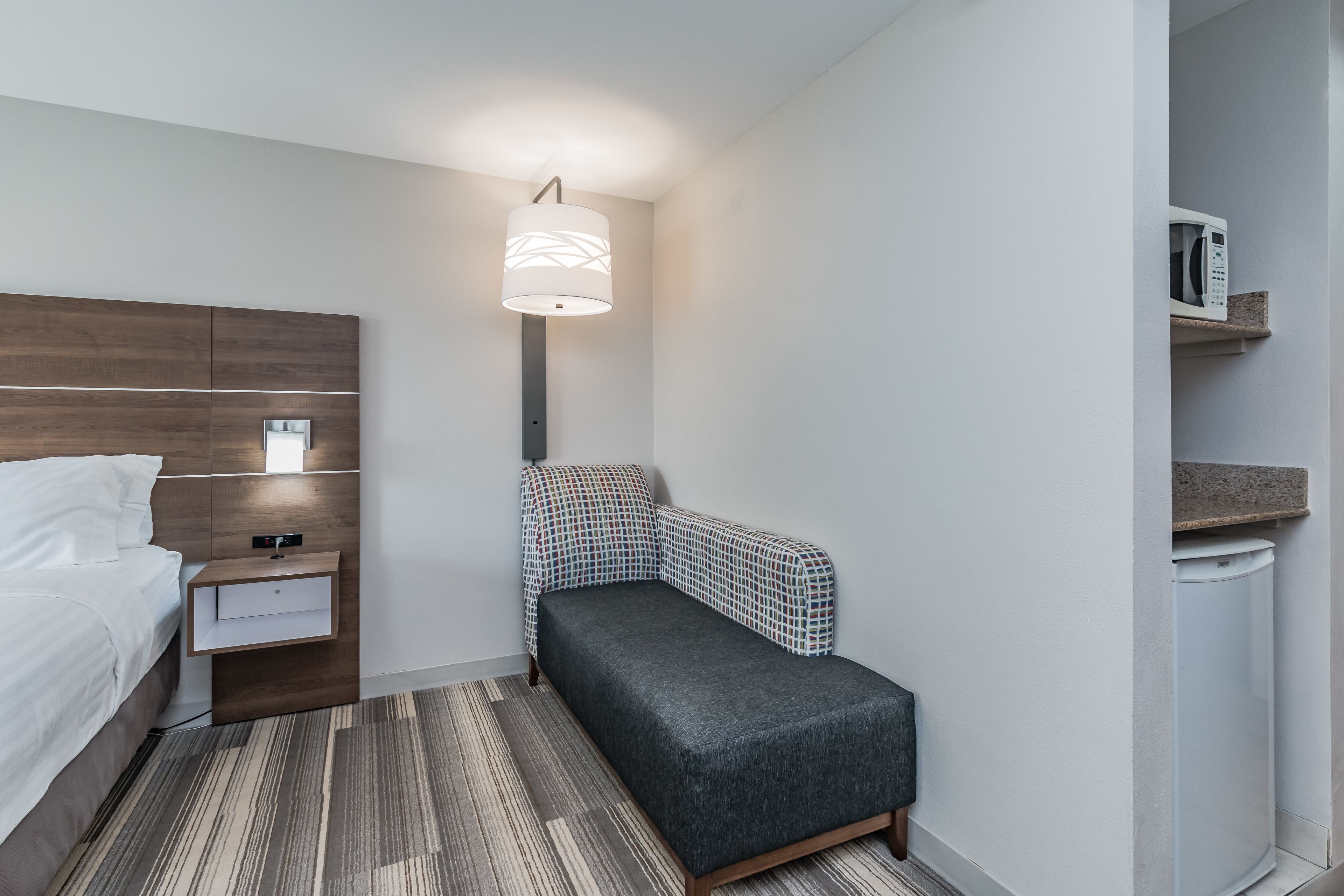 Une chambre d’hôtel de taille réduite, comprenant un lit, une table de chevet, une lampe et un petit canapé.