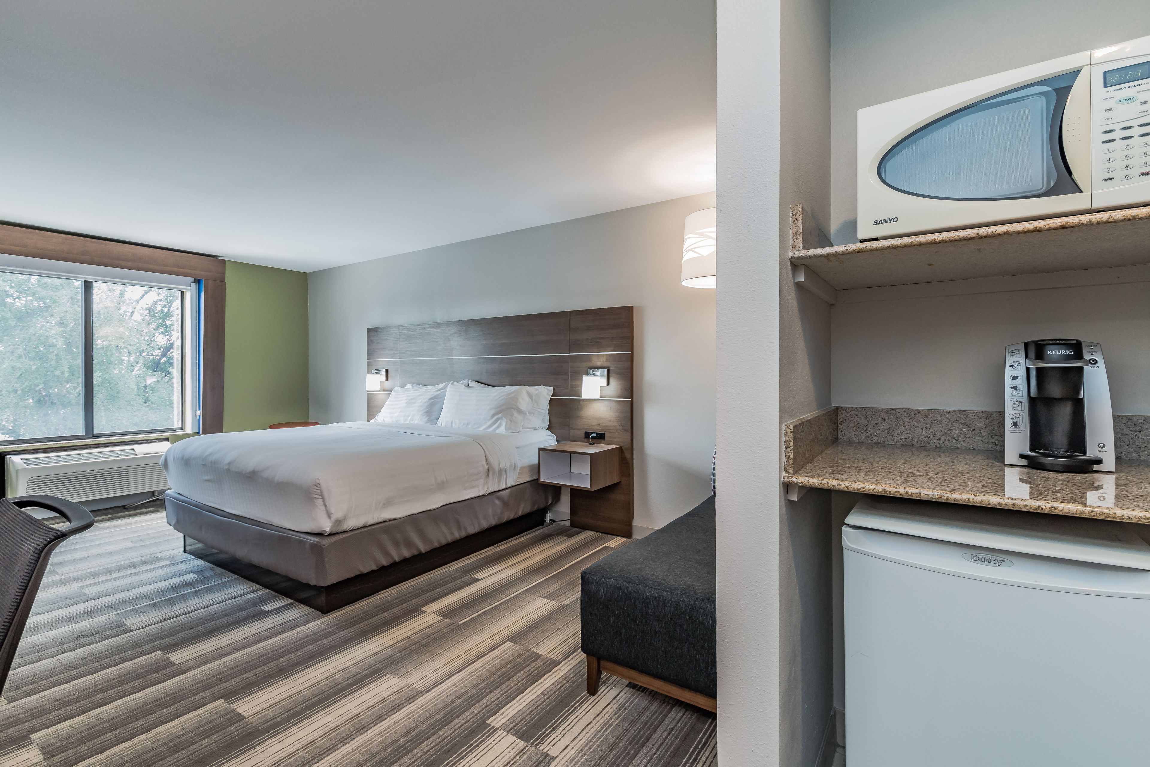 A hotel room with a bed, a nightstand, a microwave, a coffee maker, and a small refrigerator.