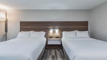 Une chambre d’hôtel avec deux lits, une tête de lit en bois, une table de chevet avec une lampe et un luminaire fixé au mur.