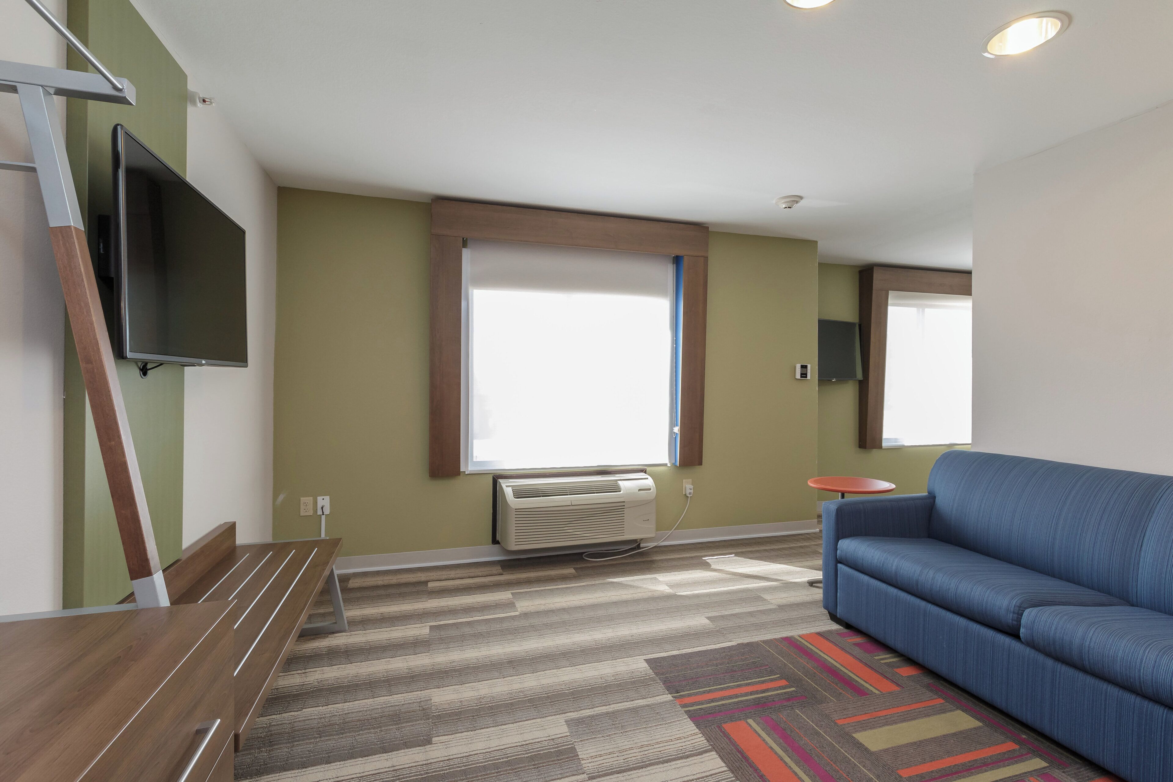 A modern living room with a blue sofa, a flat-screen TV mounted on the wall, a standing heater, and a small round table.