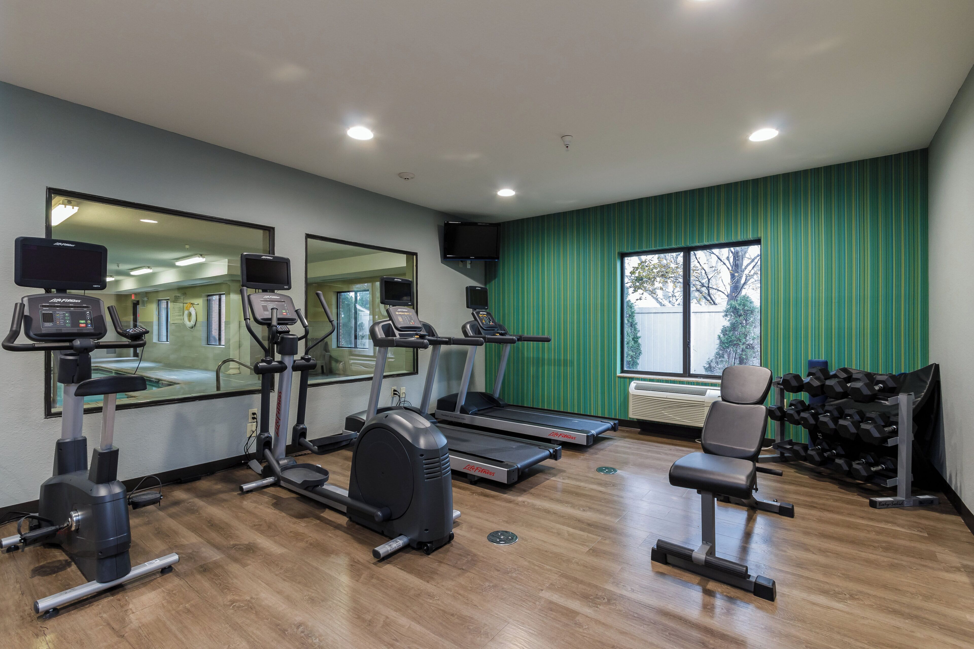 A gym with cardio machines, a mirror, and a chair.