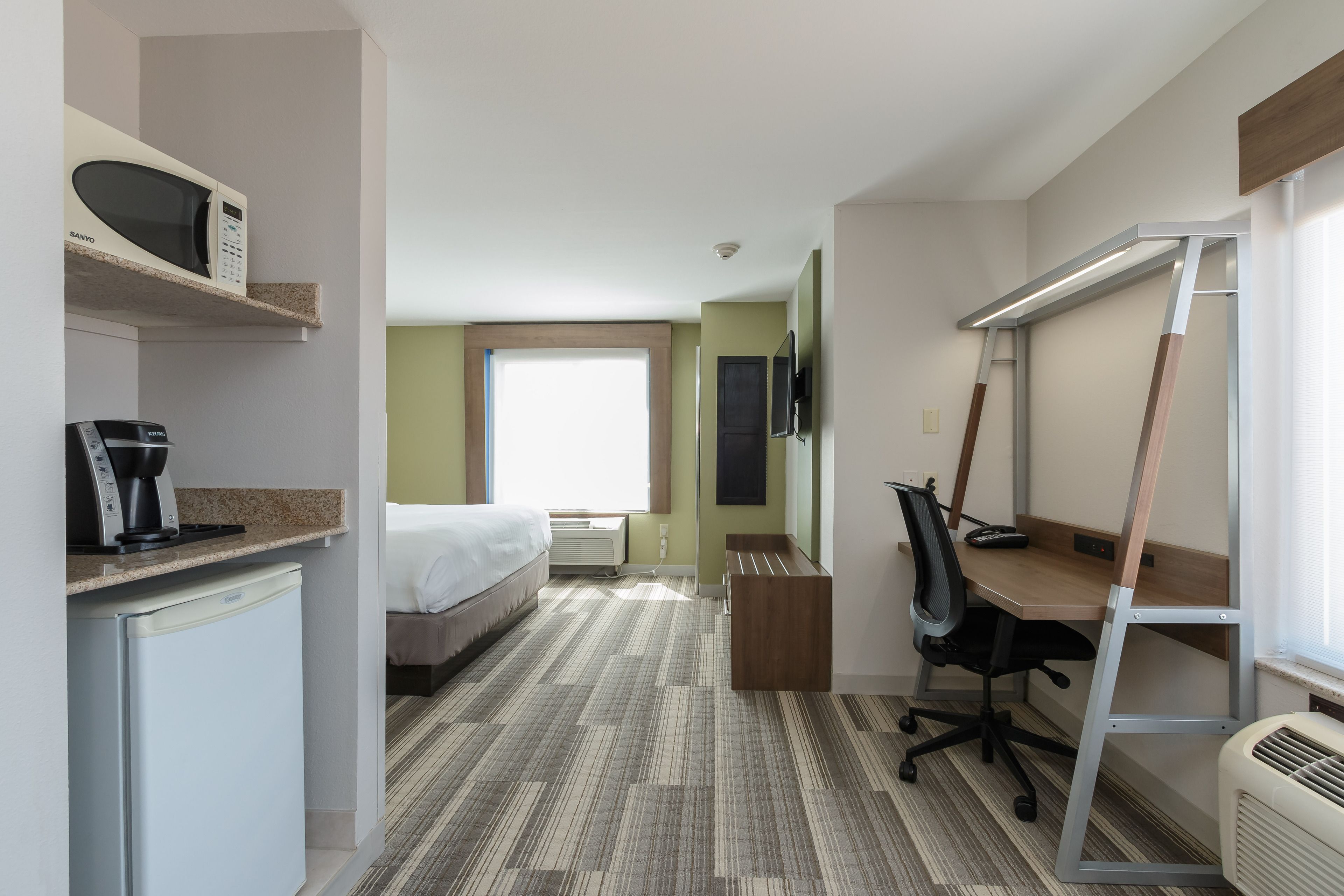 A hotel room with a bed, a desk with a chair, a microwave, a coffee maker, and a TV.