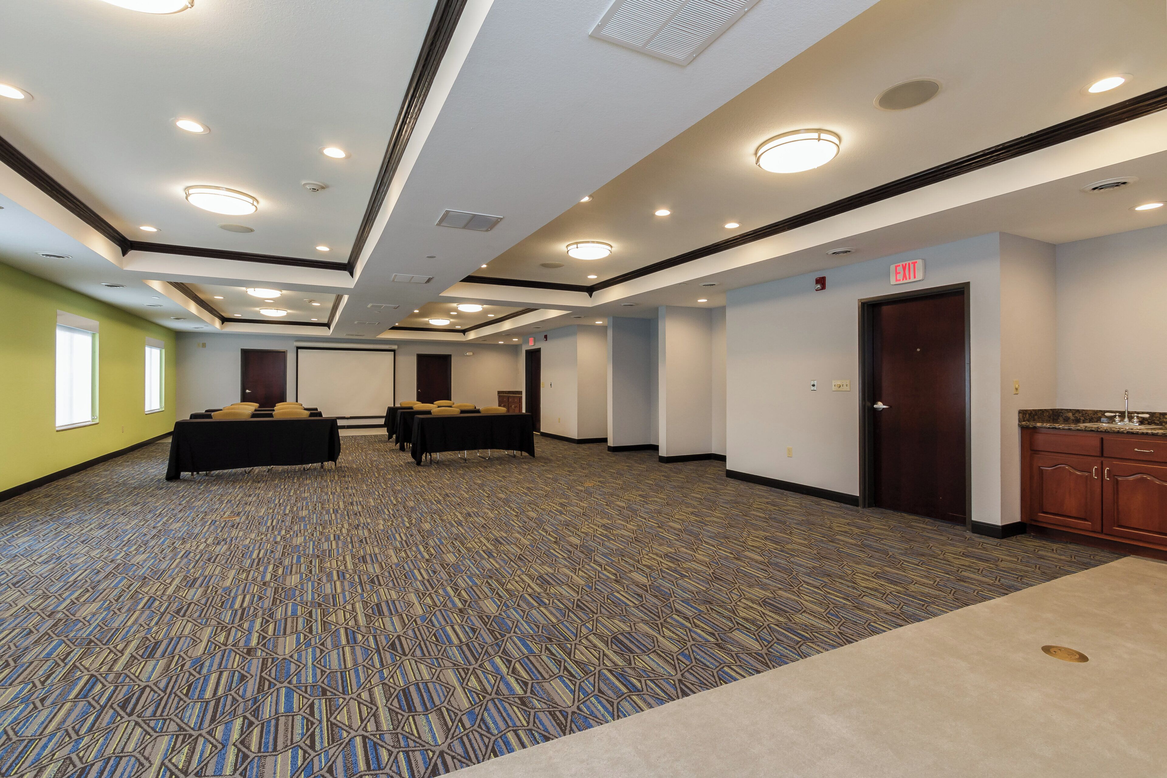 Un salón de conferencias con mesas, sillas, una kitchenette y una puerta de salida.