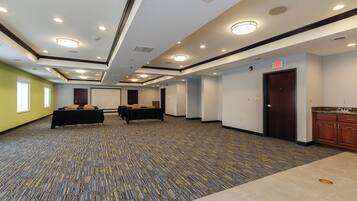 Un salón de conferencias con mesas, sillas, una kitchenette y una puerta de salida.