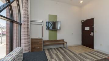Una habitación de hotel con cama, un banco, un televisor, una puerta y una ventana con cortinas.