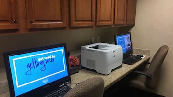 A hotel office with a desktop computer, a laptop, and a printer on a desk.