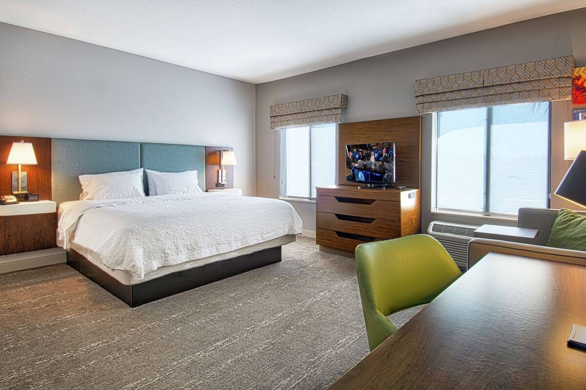 A hotel room with a large bed, a desk, a chair, a TV, and a window with a view.
