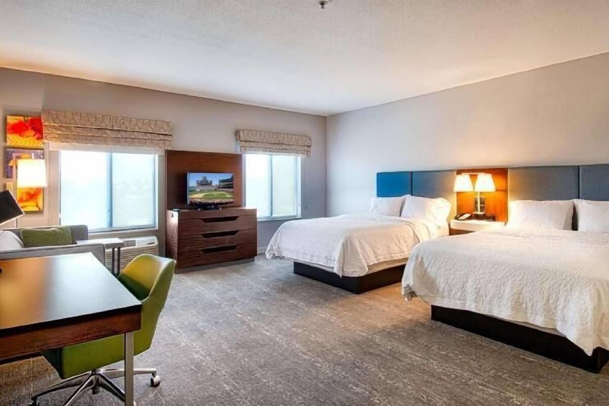 A hotel room with two beds, a desk, a chair, a TV, and a window.
