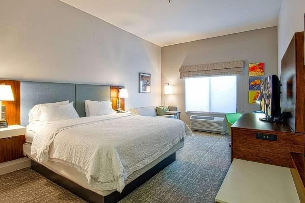 A hotel room with a large bed, bedside lamps, a flat-screen TV, a desk, and a window with a view.