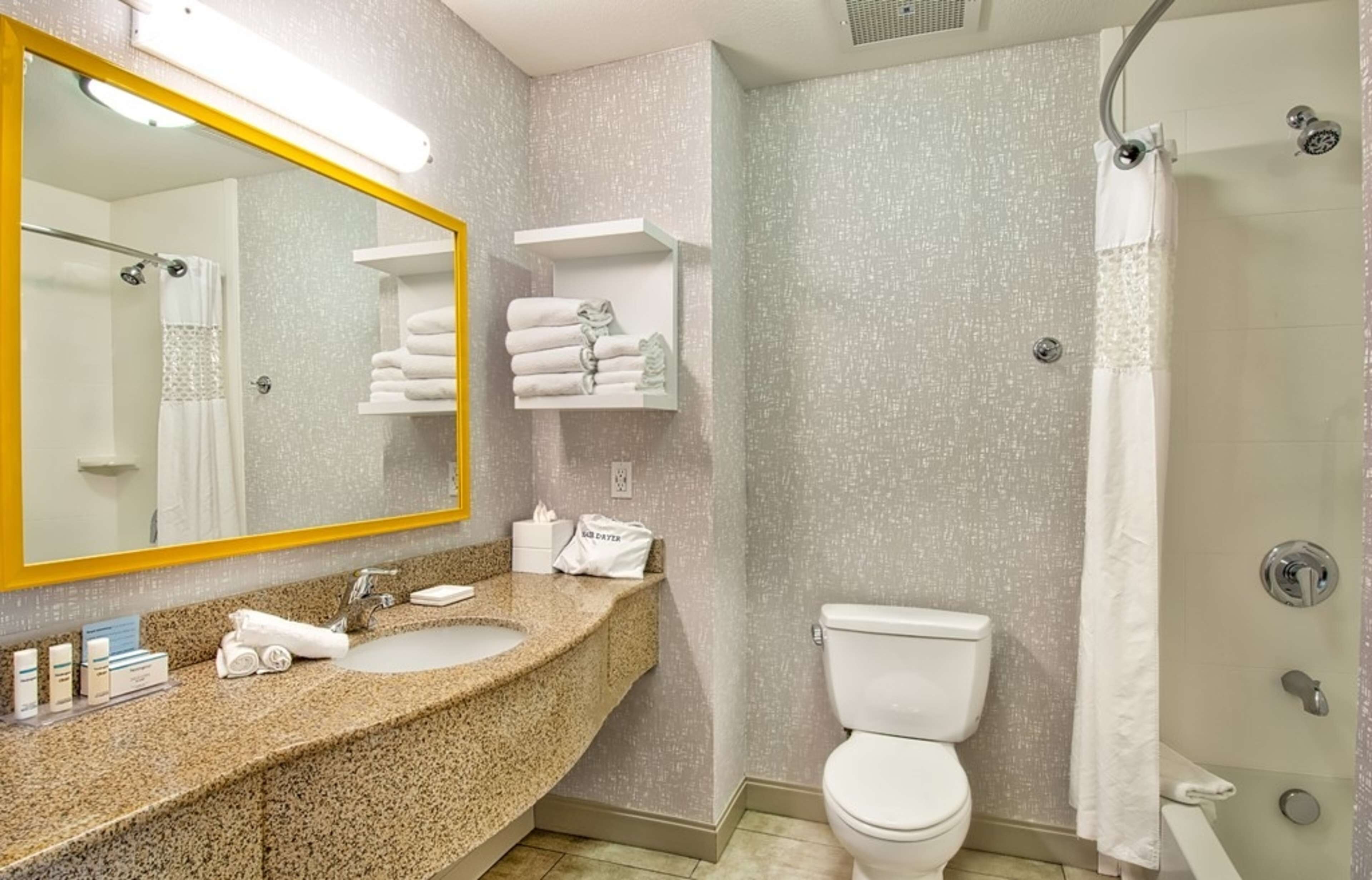 Un baño con lavamanos de granito, inodoro blanco, ducha con puerta de cristal y toallero con toallas dobladas.