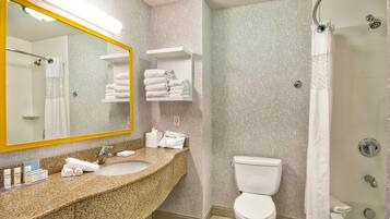 Un baño con lavamanos de granito, inodoro blanco, ducha con puerta de cristal y toallero con toallas dobladas.