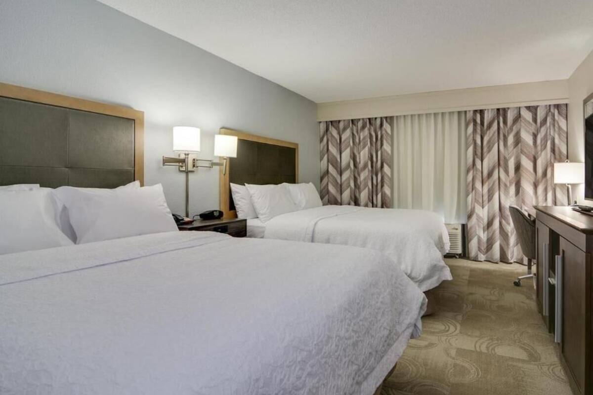 A hotel room with two beds, a desk, a chair, and a window with curtains.