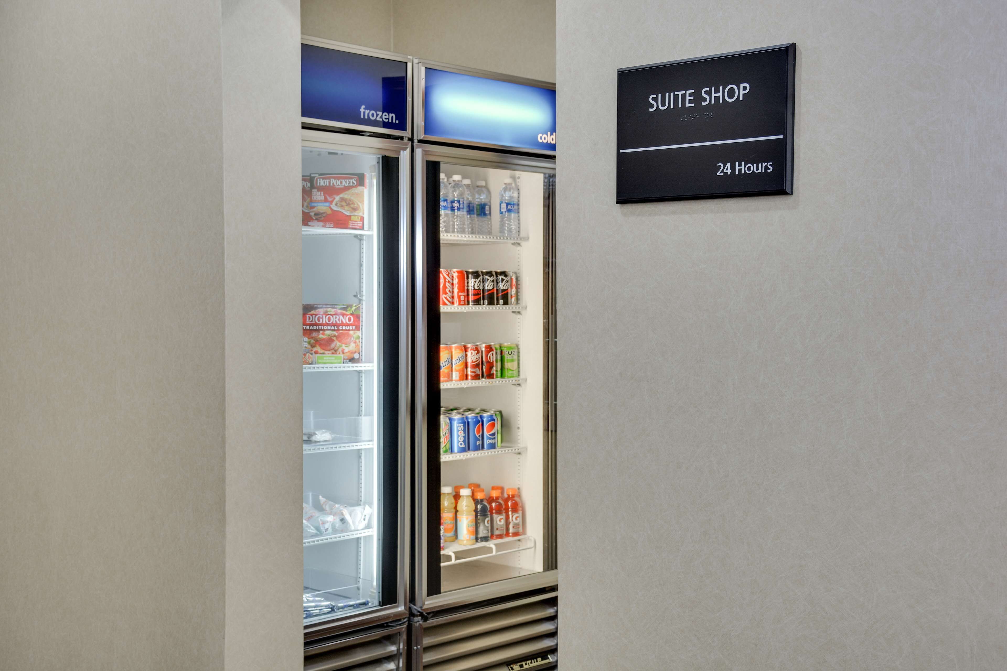 Tienda de suites con letrero disponible las 24 horas y dos refrigeradores llenos de diversas bebidas.
