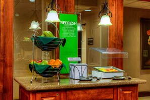 Un área de desayuno de hotel con un frutero, un letrero de precaución y un cartel verde que anuncia servicios de fruta fresca: pelar, servir, cortar y relajarse.