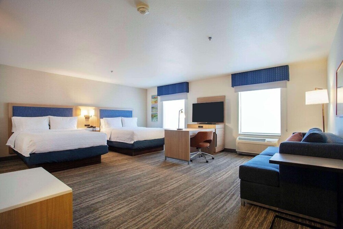 A hotel room with two beds, a desk, a chair, a couch, and a TV.