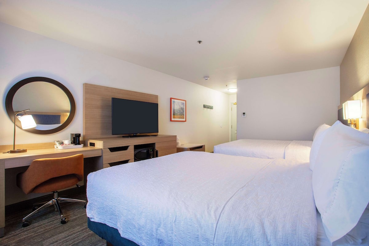 Quarto de hotel com uma cama grande, uma escrivaninha com computador, televisão e um espelho redondo.