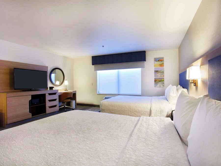 Hotelkamer met een groot bed, een televisie, een bureau, een stoel, een raam en een wandlamp.