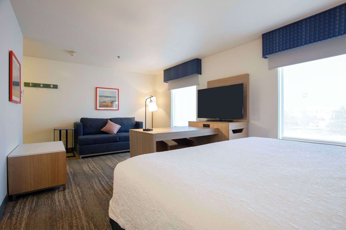 Quarto de hotel com uma cama grande, uma escrivaninha, uma televisão, um sofá e uma janela com vista para a cidade.