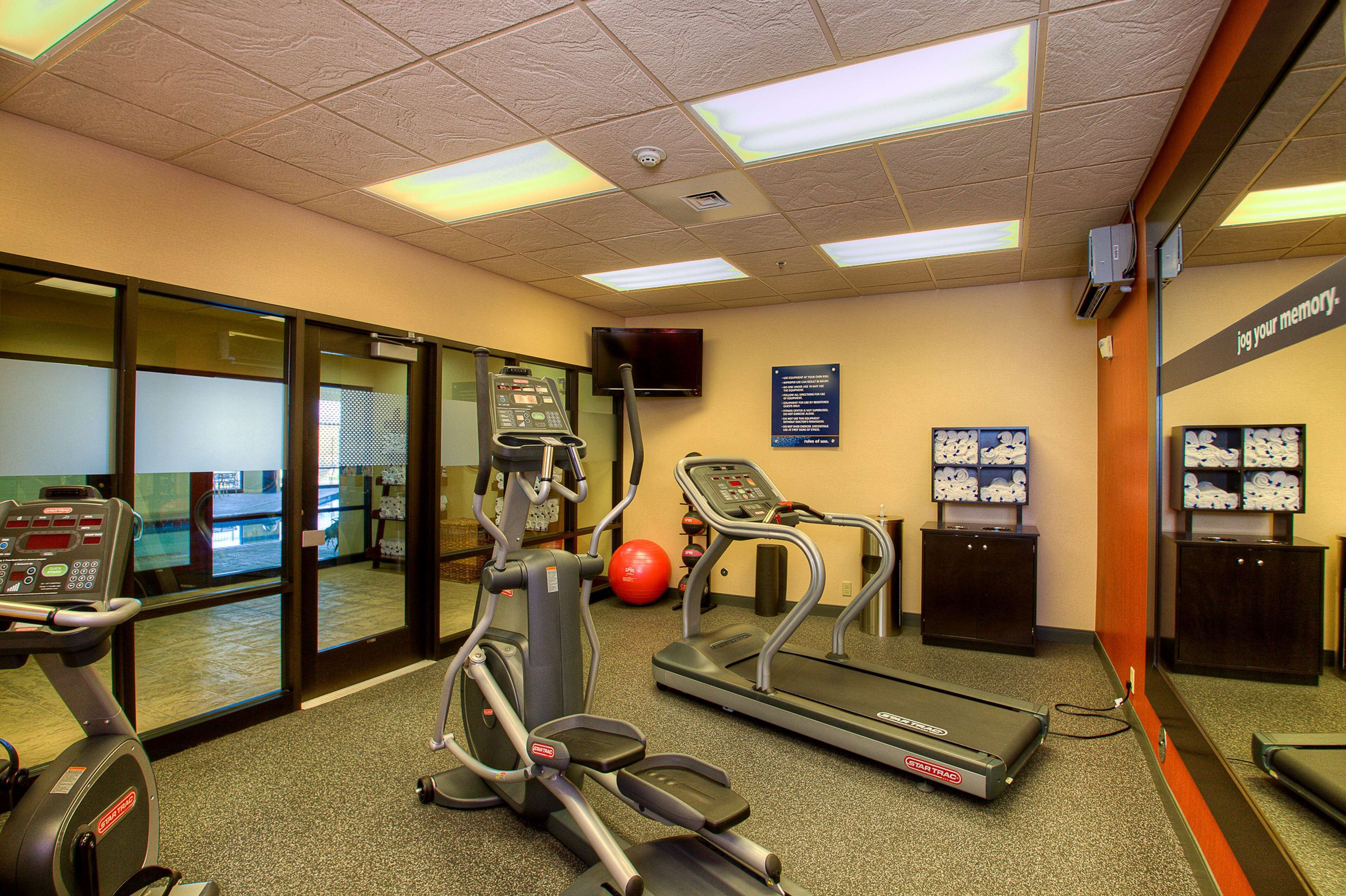 Une salle de sport équipée de tapis de course, d’un vélo elliptique, d’un vélo d’appartement et d’un ballon d’exercice rouge.