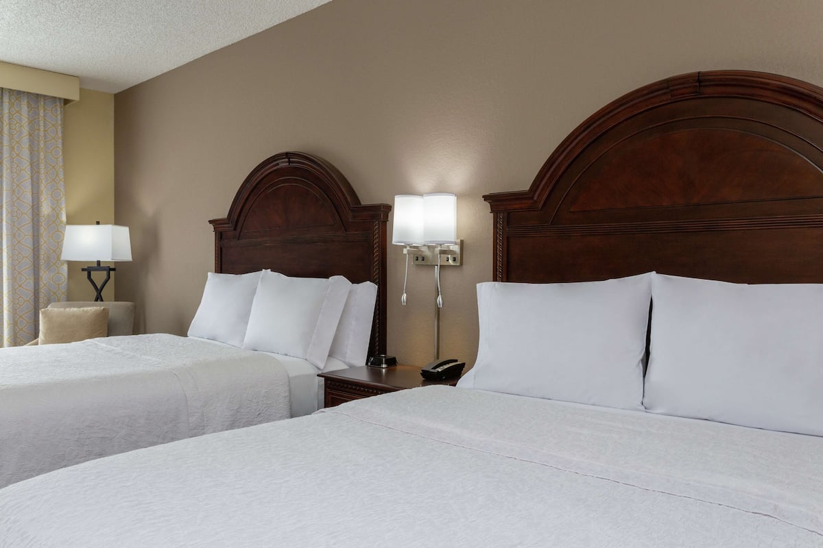 A hotel room with two beds, a wooden headboard, bedside lamps, and a nightstand with a phone.
