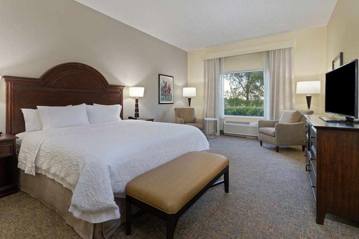 A hotel room with a large bed, a desk with a TV, a chair, and a window with curtains.