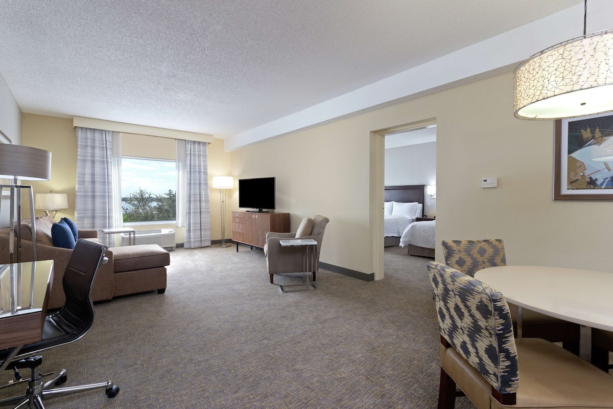 A hotel room with a sofa, armchair, dining table, and a television.