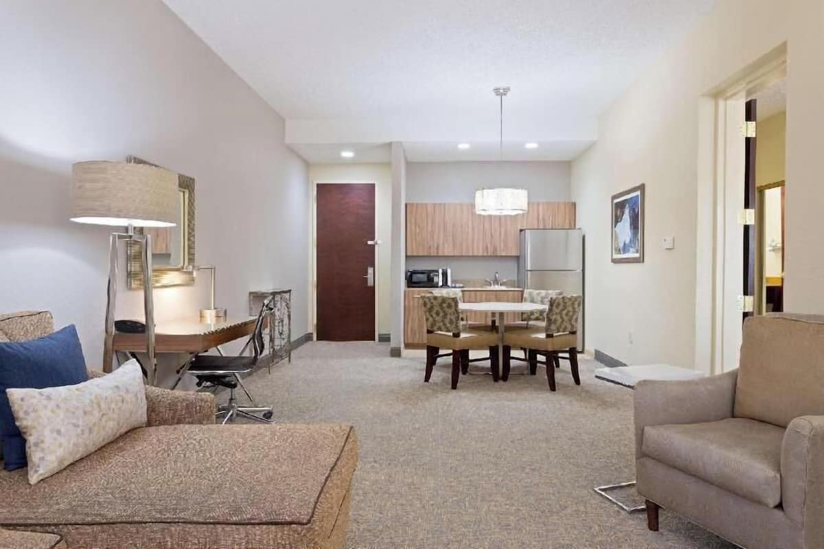 A modern living room with a sofa, a dining table with chairs, a kitchen area, and a door leading to another room.