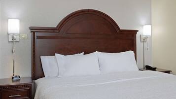 A hotel room with a wooden headboard, white bedding, a bedside table with a lamp, and a phone on the nightstand.