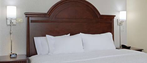 A hotel room with a wooden headboard, white bedding, a bedside table with a lamp, and a phone on the nightstand.